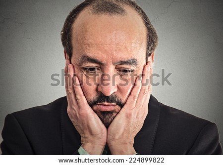 Closeup portrait very sad, depressed, alone, disappointed upset man resting his face on hand looking down isolated on grey wall background. Human mood expression, emotions, feeling, life perception