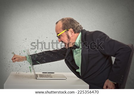 furious businessman throws a punch into computer screaming isolated grey office wall background. Negative human emotions, facial expressions, feelings, aggression, anger management issues concept