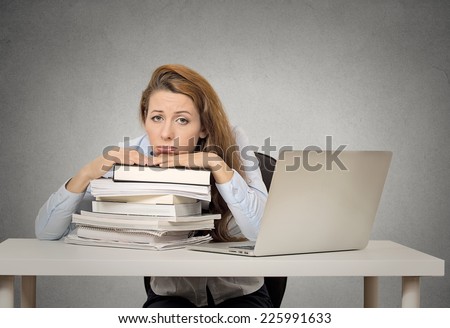 Demotivated female student sitting in at desk with pile of books and computer bored tired funny looking isolated on grey wall blackboard background. Human face expression emotion feeling bad attitude