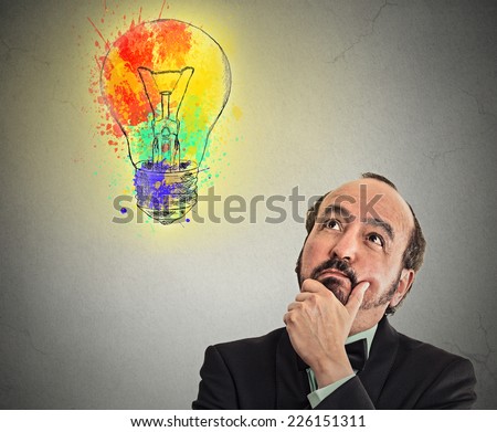 Middle aged business man with thoughtful expression and light bulb over his head looking up thinking isolated grey wall background. Human emotions perception