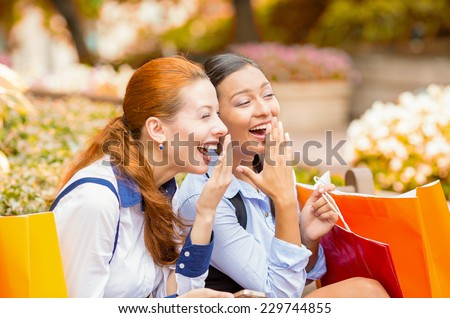 Closeup portrait two laughing happy looking girls discussing latest gossip news. Young shopping women outside in park sitting on bench. Positive face expressions, emotions, feelings, body language