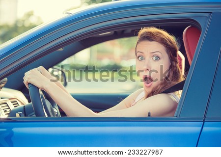 Distracted fright face of a woman driving car, wide open mouth eyes holding wheel side window view. Negative human face expression emotion reaction. Trip risk danger reckless behavior on road concept