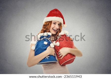 Young happy santa helper in red hat holding gift sacks isolated on grey wall background with copy space. Positive face expression. Santa claus is coming. Holiday season concept
