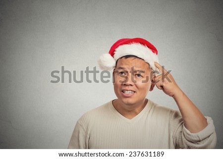 closeup headshot xmas man with red santa claus hat looking up scratching head thinking of gift idea for holiday isolated grey wall background with copy space Human face expression emotion perception