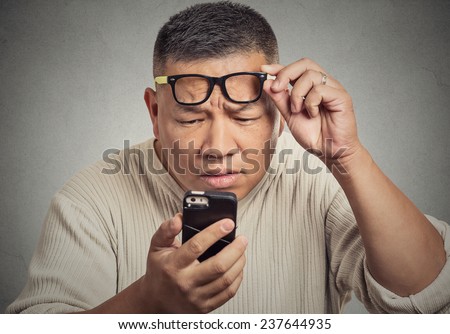 Closeup portrait headshot middle aged man with glasses having trouble seeing cell phone screen because of vision problems. Bad text message. Negative human emotion facial expression feeling perception