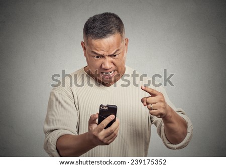 Closeup portrait angry middle aged man, guy, mad worker, pissed off employee while on mobile, pointing with finger at his smart phone isolated grey wall background. Negative emotion facial expression
