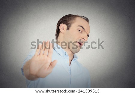 Closeup portrait young handsome grumpy man with bad attitude giving talk to hand gesture with palm outward isolated grey wall background. Negative emotion, facial expression feelings body language