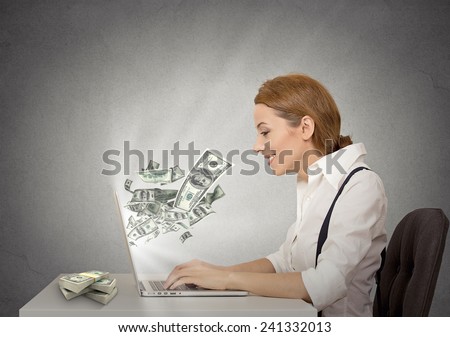 Side profile happy smiling business woman working online on computer earning money dollar bills banknotes flying out of laptop screen isolated grey wall office background. Human face expression