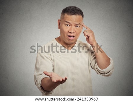 Closeup portrait angry frustrated middle aged man gesturing with his finger against temple asking are you crazy? Isolated grey wall background. Human face expression emotion body language attitude