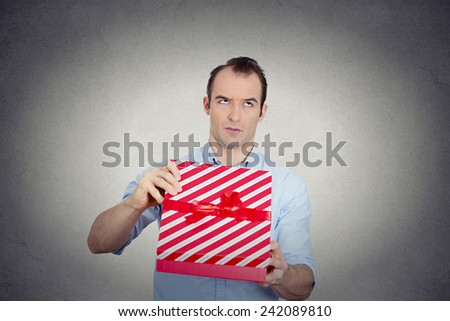 Closeup portrait grumpy unhappy upset man holding red gift box very displeased with what he received, disgust on face isolated grey background. Negative emotion facial expression feeling attitude