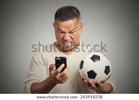 Portrait angry frustrated man looking on cell smart phone watching game holding football displeased isolated grey wall background. Negative emotion, face expression feelings. Data plan online gaming
