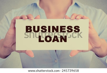 Business woman hands holding white card sign with business loan text message isolated on grey wall office background. Retro instagram style image