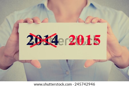 Businesswoman hands holding white card sign with year 2014 crossed and 2015 marked in red message isolated on grey wall office background. Retro instagram style image