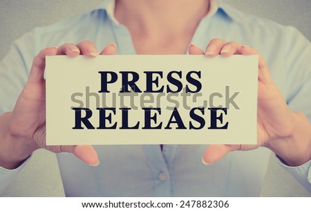 Businesswoman hands holding white card sign with press release text message isolated on grey wall office background. Retro instagram style image