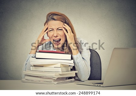 Too much work tired stressed young woman sitting at her desk with books in front laptop computer isolated grey wall office background. Busy college schedule burnout workplace sleep deprivation concept