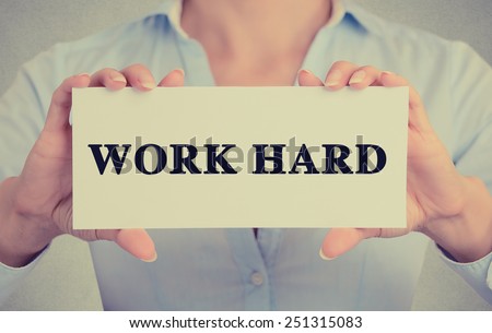 Closeup businesswoman hands holding white card sign with work hard text message isolated on grey wall office background. Retro instagram style image