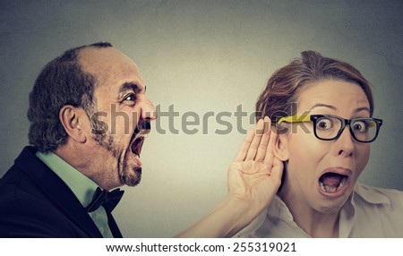 Can you hear me? Portrait angry man screaming curious surprised woman with glasses and hand to ear gesture listens isolated on grey wall background. Human face expressions