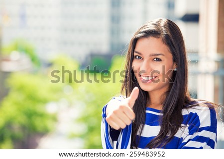 Happy beautiful woman with thumbs up isolated on city background. Positive face expression life perception