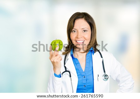 Happy smiling female doctor with green apple standing in hospital hallway