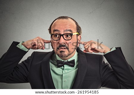 Annoyed mature man with glasses plugging ears with fingers isolated on gray wall background