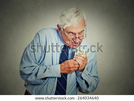 Closeup portrait greedy senior executive, CEO, boss, old corporate employee, mature man, holding dollar banknotes isolated on gray wall background. Negative human emotion facial expression