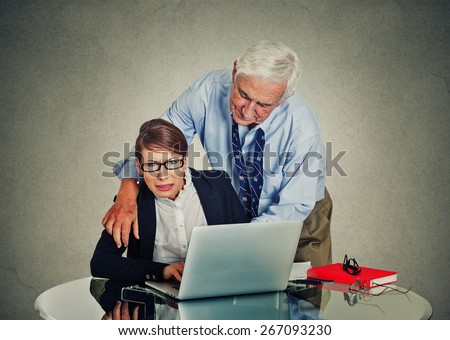 Senior elderly businessman harassing his young colleague at work isolated on gray office wall background