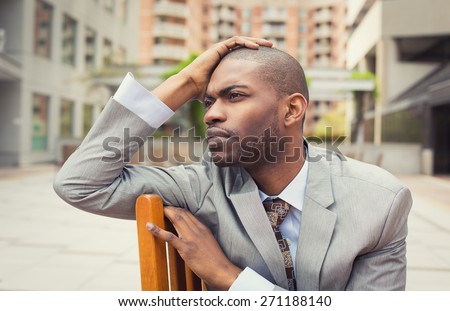 Stressed young businessman sitting outside corporate office. Negative human emotion facial expression feelings.