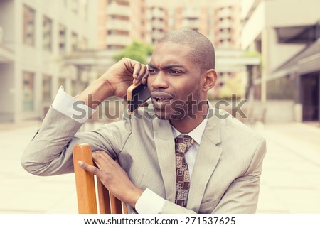 Closeup portrait unhappy upset sad, skeptical man talking on phone sitting outdoors isolated office background. Negative human emotion facial expression feeling, life reaction. Bad news