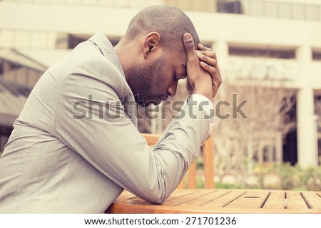 side profile stressed young businessman sitting outside corporate office holding head with hands looking down. Negative human emotion facial expression feelings.