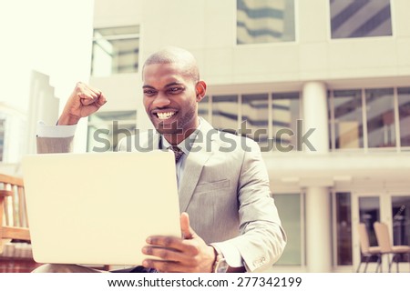 Happy successful young man with laptop computer celebrates success outside corporate office