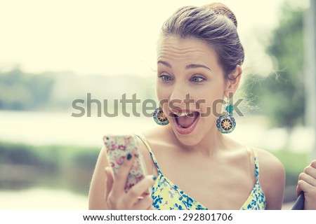 Closeup portrait surprised screaming young girl looking at phone seeing news or photos with funny emotion on her face isolated outside city background. Human emotion, reaction, expression