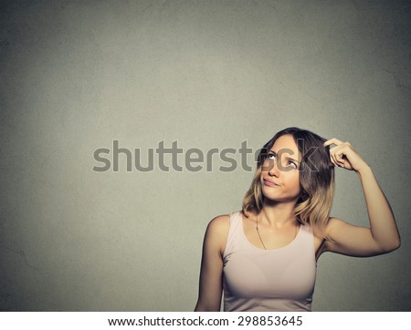 Closeup portrait headshot young woman scratching head, thinking daydreaming deeply about something looking up isolated on gray wall background. Human facial expression emotion feeling sign symbol