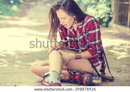in-line skating injured young woman suffering from pain sitting on the ground touching painful knee waiting in need for medical help outdoors on summer day