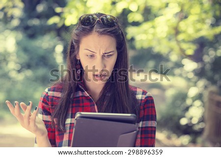Portrait upset sad skeptical unhappy serious woman using mobile pad computer displeased with email news she received isolated park trees background. Negative human emotion face expression feeling