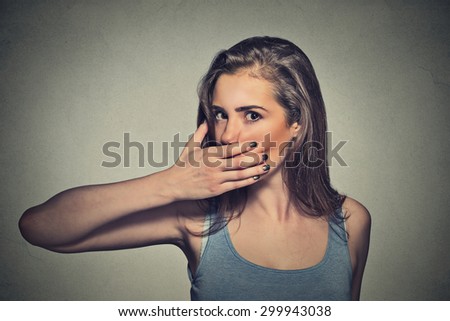 Closeup portrait of scared young woman covering with hand her mouth isolated on gray wall background