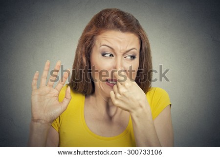 Closeup portrait young woman disgusted by smell looks displeased, something stinks, bad odor situation isolated on gray wall background. Human face expression body language, perception, senses