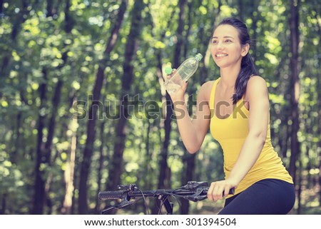 Young happy woman on bike standing on a hill road enjoying beautiful view summer sunny day resting drinking water