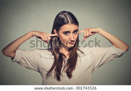Closeup portrait young angry unhappy woman with closed ears looking at you annoyed by loud noise giving her headache ignoring isolated on gray wall background. Negative emotion perception attitude