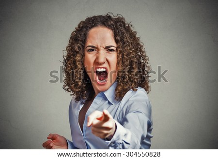 Portrait angry young woman pointing finger at camera screaming isolated on grey wall background