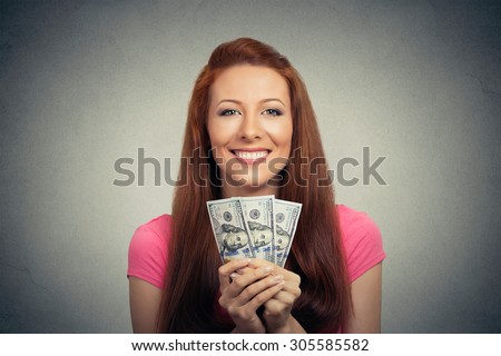 Closeup portrait super happy excited successful young business woman holding money dollar bills in hand isolated grey wall background. Positive emotion facial expression feeling. Financial reward