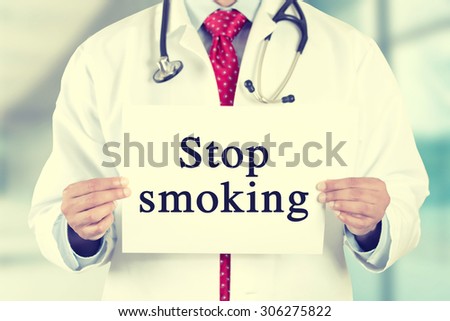 Closeup doctor hands holding white card sign with stop smoking text message isolated on hospital clinic office background. Retro instagram style filter image