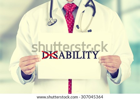 Closeup doctor hands holding white card sign with disability crossing through the Dis with a red marker text message isolated on hospital clinic office background. Retro instagram style filter image