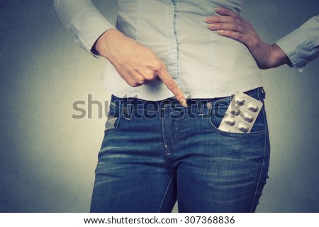 Closeup cropped image of a woman pointing with finger at pills in her pocket on gray background