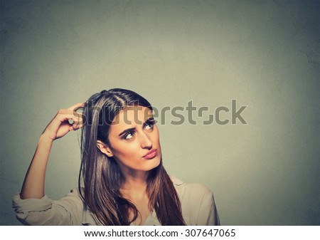 Contused thinking woman bewildered scratching her head seeks a solution isolated on gray wall background. Young woman looking up