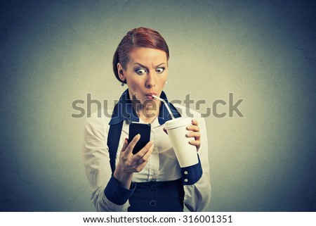 Closeup portrait surprised business woman reading breaking news on smart phone drinking soda coffee isolated on grey wall background. Human face expression, corporate executive emotions