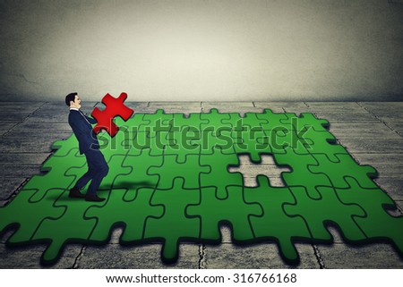 young business man holding carrying last piece of green puzzle