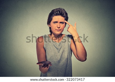 Closeup portrait of angry mad young woman gesturing with her finger against temple asking are you crazy? Isolated on gray wall background. Negative emotions facial expression feeling body language