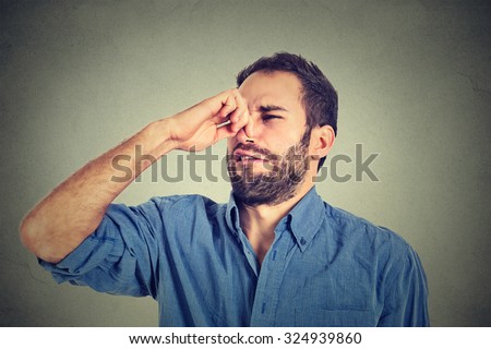 portrait of disgusted man pinches nose with fingers hands looks with disgust something stinks bad smell situation isolated on gray wall background. Human face expression body language reaction