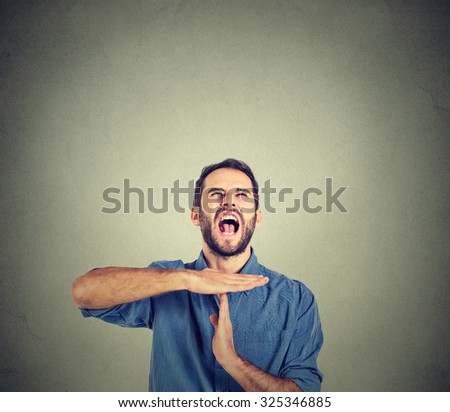 Young man showing time out hand gesture, frustrated screaming to stop isolated on grey wall background. Too many things to do. Human emotions face expression reaction
