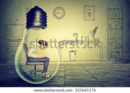 Side profile young woman using working on computer sitting inside electric lamp in her corporate office on a gray wall background. Generate idea concept